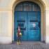 A woman in a dress stands in front of a blue door in Munich