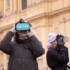Two women stand in front of the Theatinerkirche in Munich in winter wearing VR glasses of TimeRide Go.