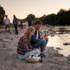 A man and a woman sit in the sunset by the Isar and drink a beer.
