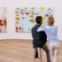 Un hombre en cuclillas y una mujer de pie frente a unos cuadros en el Museo Brandhorst de Múnich. Los dos miran juntos los cuadros, mientras la mujer se apoya en el hombro del hombre.