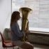 A blonde woman sits on a chair and plays the tuba