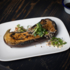 A grilled aubergine with herbs served on a white plate