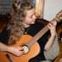 A woman with long hair plays the guitar on a sofa.