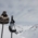 Two ski poles with woolly hats are stuck in the snow in front of a winter mountain panorama.