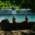 Two men in swimming trunks sit on a wall overlooking the Isar river