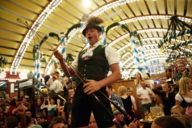 A man dressed in a traditional costume is celebrating and dancing on a table in a beer tent at the Oktoberfest in Munich.