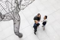 Two women and a man are talking besides a huge sculpture in Munich.