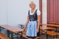 A woman who is wearing a dirndl is standing in front of a tent at the Oktoberfest in Munich.