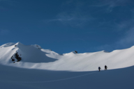 Two ski tourers on their way to the summit against a blue sky.