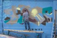 Photo of an artist painting on a large brick wall in Munich.