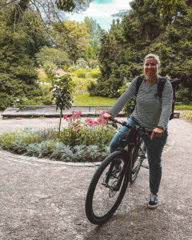 A woman stops in a garden area with her mountain bike.