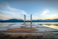 Una passerella di legno con scala sul lago Tegernsee con vista sul tramonto dietro le Prealpi bavaresi vicino a Monaco.