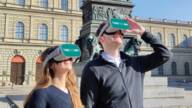 Guests of the TimeRide wear VR glasses in front of the Residenz in Munich.
