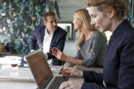 Two women and a man working at at table with a laptop in a hotel in Munich.