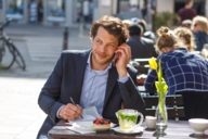 A man is sitting in a street cafe and is phoning at Gärtnerplatz in Munich.