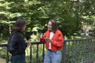 Two women stand with microphones on a bridge in the green and talk.