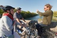 Three cyclists are talking to each other on a bridge at the Isar River in Munich.