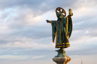 Statue of the Münchner Kindl - name and symbol of the coat of arms of Munich - on top of the Neues Rathaus tower photographed from the air with a drone with the Frauenkirche in the background.