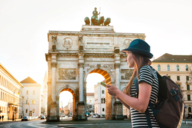 A woman stands in front of the Siegestor in Munich with a smartphone in her hand.