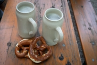 Two beer mugs and two pretzels on a wooden table.