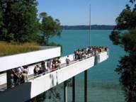 The footbridge of a modern building serves as a viewing platform high above a lake.