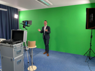 A man stands in front of a greenwall and talks into the camera.