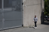 A man in sunglasses walks along a wall in Munich and laughs.