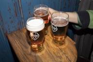Three beer glasses on a wooden table and a person reaches for them.