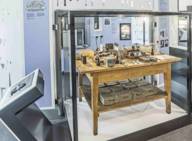 Tavolo di legno con numerosi strumenti di laboratorio in una teca di vetro.