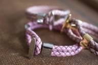 A pink bracelet from the Enzo Escoba brand lies on a brown background.