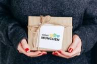 A woman with varnished fingernails holds a gift with the inscription "simply Munich".
