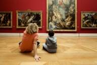 Un jeune homme et un garçon sont assis par terre dans la salle Rubens de l'Alte Pinakothek à Munich et regardent des tableaux.