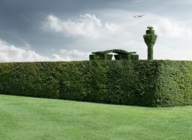 A green hedge with a planted airport tower in the background.