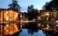 View from a swimming pond into illuminated, glazed sauna areas during the blue hour.