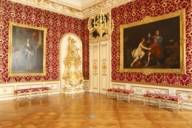 A red and gold room in the residence with large paintings and antique furniture