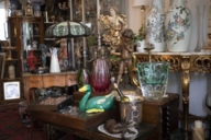 Antique statues and vases stand amidst antique furniture and old lamps