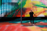 A blond young man in portrait in front of colourful fluorescent tubes