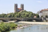 Des personnes se baignant et prenant des bains de soleil au bord de la rivière Isar à Munich avec l'église St Maximilien en arrière-plan.