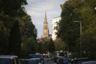 A tree-lined street with cars on its sides running towards a Heilig-Kreuz- Kirche church in Giesing district in Munich.