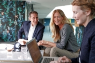 A man and two women are sitting at a table with a laptop in a hotel in Munich.