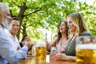 Two men and two women are sitting on a bench in a beer garden in Munich.