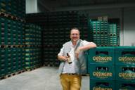 Steffen Marx stands in front of crates of beer of Giesinger Bräu with a bottle of beer in his hand.