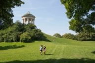 Two women are walking on the meadow under the Monopteros in the Englischer Garten in Munich.