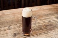 Une bière brune dans un verre étroit sur une table en bois