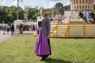 A woman who is wearing a dirndl is standing in front of a carousel at the Oktoberfest in Munich.
