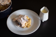 A dessert with icing sugar on a plate beside a pot with vanilla sauce