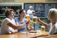 Three tourists are having a toast with beer mugs.