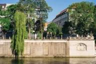 View from the river to a stone wall and trees during summertime in Munich