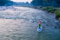 A man is standing on a stand up paddle board on the river Isar in Munich photographed from above with a drone.