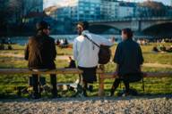 Trois personnes sont assises au soleil couchant au bord de l'Isar à Munich et l'un d'entre eux joue de la guitare.